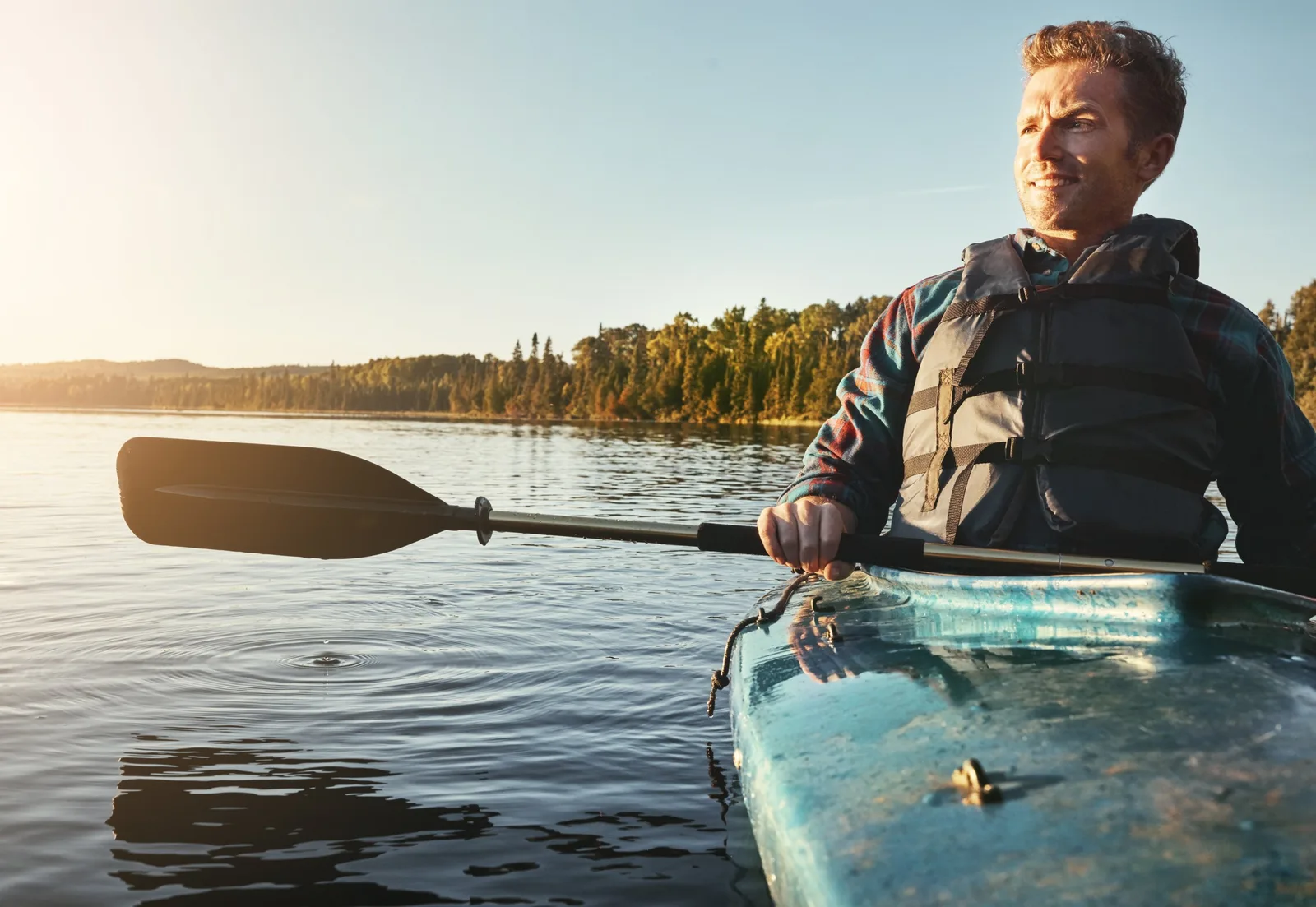 Nybörjare paddlar kajak nära land med flytväst i lugnt nordiskt vatten